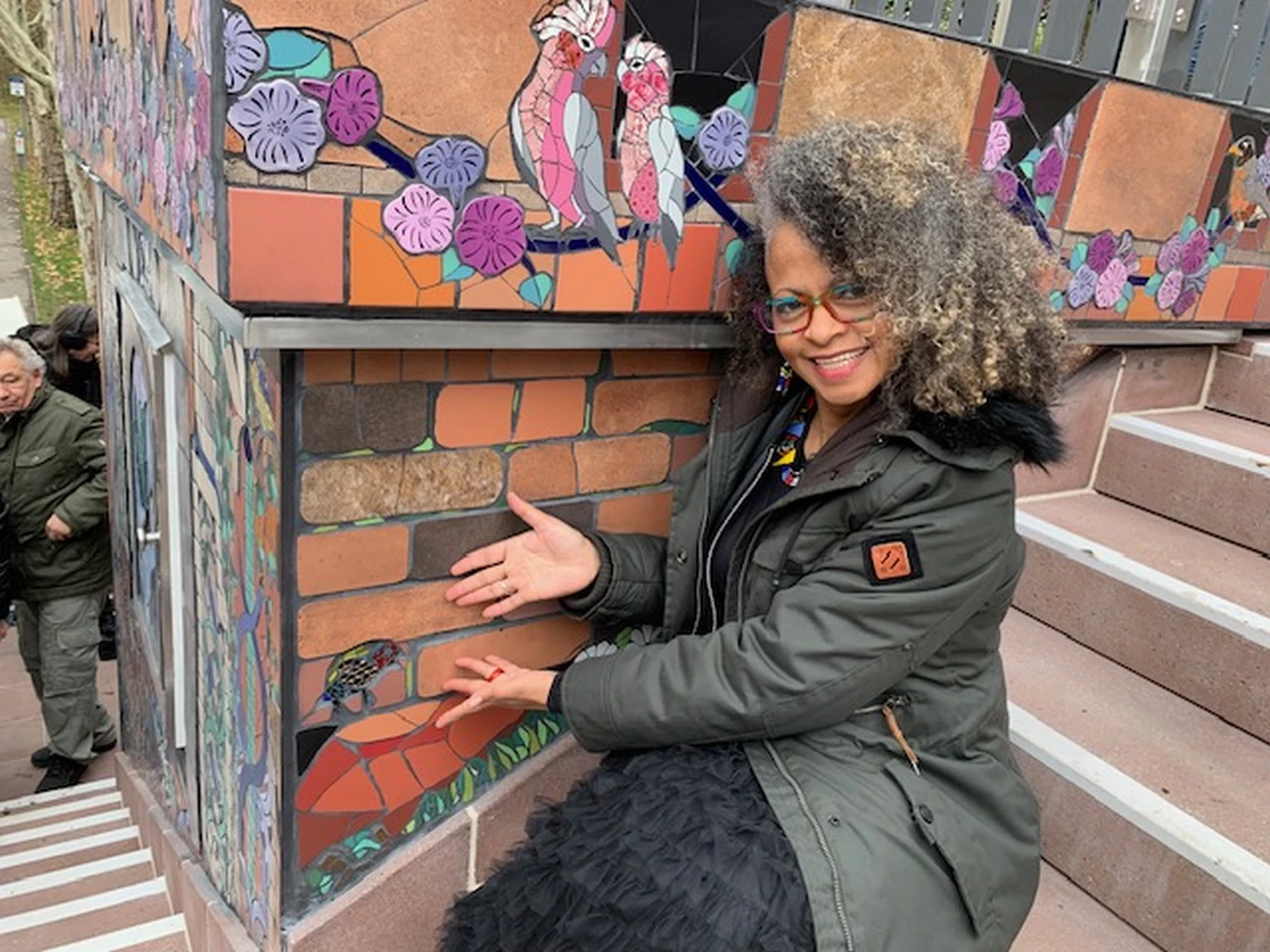 Natlie pointing towards mosaic art on a wall